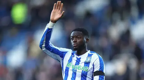 Dominic Iorfa in the blue and white striped shirt of Sheffield Wednesday waves to the crowd.