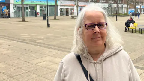 Shariqua Ahmed/BBC Karina wearing a beige zipped hoodie smiling at the camera 