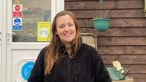 BBC/ Eve Kennedy A woman with long brown hair, wearing a black fleece, stands outside a rescue centre.