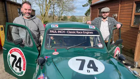 Two men stood either side of a green classic racing car