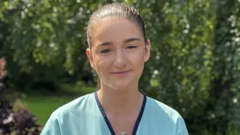 Kate McMullan, a woman with dark hair, who is wearing a green top with a blue collar.