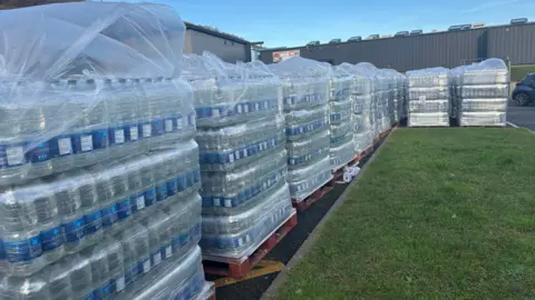 Large piles of bottles of water are stacked on pallets 