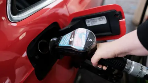 A woman fills a red car with diesel from the pump.