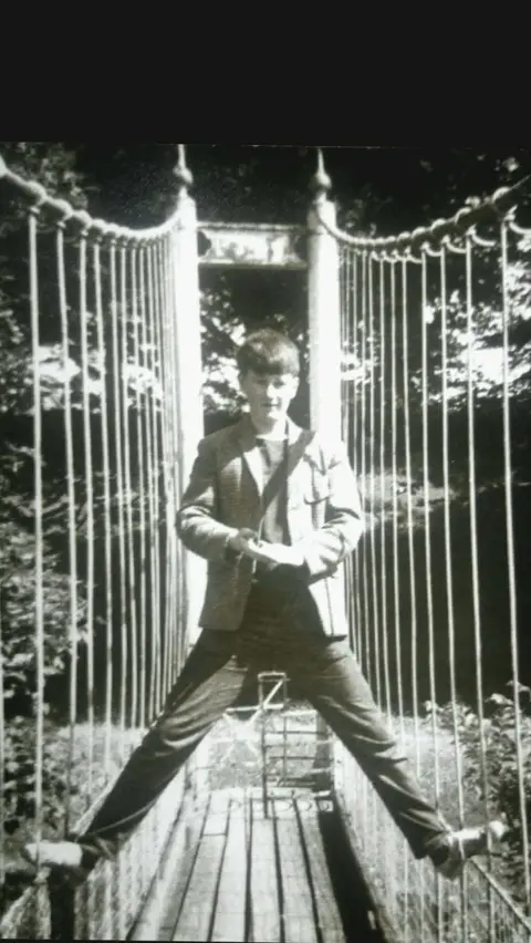 Neil Sharkey A black and white image of a young boy with his feet standing on either side of the railings of the Diamond Jubilee bridge 