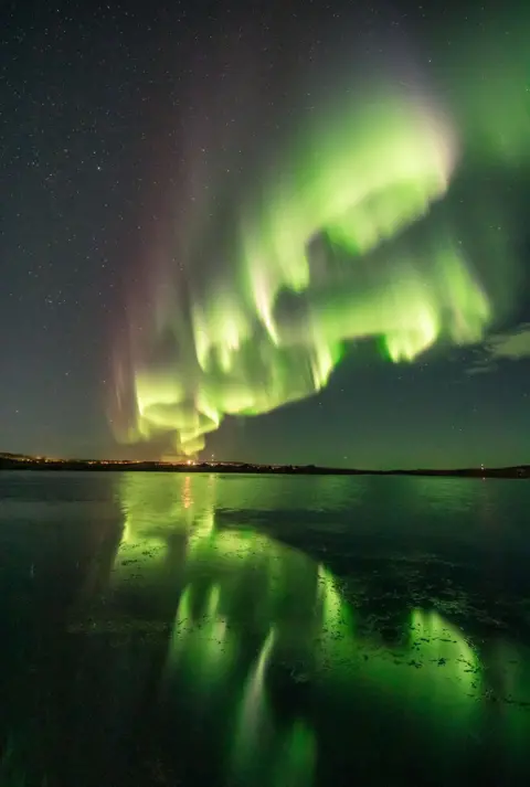 Alexander Kuznetsov / Reuters Green and purple lights from the aurora borealis illuminates a night sky and is reflected on water below