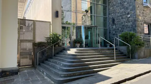 BBC Guernsey's Royal Court from the exterior. A sequence of steps, going up towards a set of glass doors. 