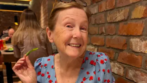 Gwent Police A woman is pictured sitting next to a brick wall wearing a dress, posing at the camera while holding a leaf.