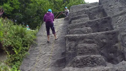 A woman wearing a purple hoody and a blue safety helmet abseiling down a rock face. 