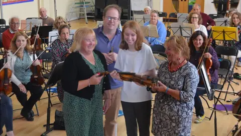 Gloucestershire Academy of Music Natasha being handed the violin by Trevor's daughters