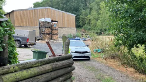 A police car is parked in front of a farm building.