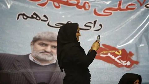Getty Images An Iranian woman takes pictures with her mobile phone in front of a portrait of Ali Motahari, a candidate for the upcoming parliamentary elections, during a campaign meeting in Tehran on February 23, 2016