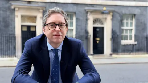 BBC Correspondent Ben Wright, wearing a blue suit and glasses outside 10 Downing Street