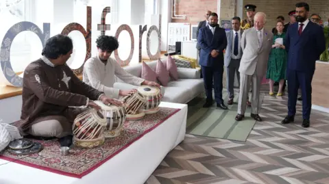 PA Media King Charles watches on as two men sit playing tabla drums.