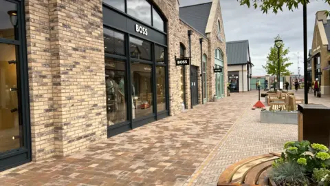 A row of brand new shops and benches and trees.