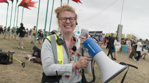 Lauren Blackburne-Tinker holding a megaphone. She is wearing glasses and smiling. She has a neon green jacket on.
