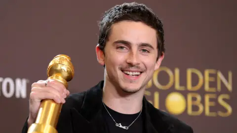 Timothée Chalamet holding up his Golden Globe and smiling