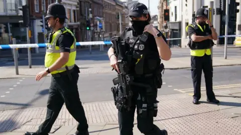 PA Media An armed officer and two unarmed police officers on patrol in Nottingham.