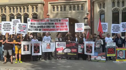 Bereaved families and friends stand in solidarity outside Arundel House in London where the Lampard Inquiry is taking place. They are all holding posters and placards of their loved ones or slogans representing why they want justice. One reads 'if mental health trusts in Essex had learned from mistakes there would only be one death instead of thousands of deaths'.