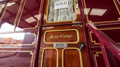 The door of a red painted caravan bearing the name Joby Carter and a white sold sign