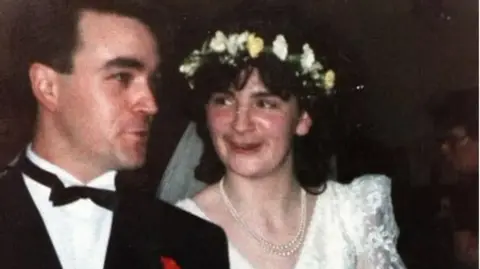 Family Handout A woman in a wedding dress, peal necklace, and a flower crown. Beside her a man wearing a suit and bow tie