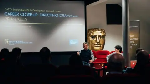Getty Images A group of people in a small cinema watching a talk or in conversation event. The big screen shows CAREER CLOSE-UP: DIRECTING DRAMA as the headline.