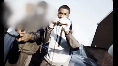 Pressplay Media A screengrab from a music video. Other people are blurred but Michael is wearing white gloves and a grey and white tracksuit. 