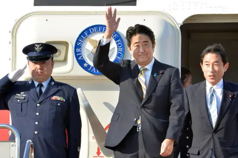 Getty Images Former Japanese Prime Minister Shinzo Abe (C), accompanied by then foreign minister Fumio Kishida (R), in 2013