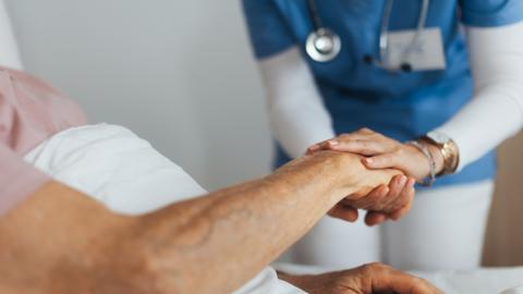 A generic image of a nurse holding an elderly person's hand while they are lying in bed
