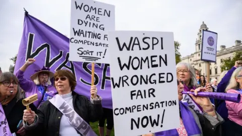 Getty Images Para pengunjuk rasa dari kelompok Perempuan Melawan Ketimpangan Pensiun Negara (Waspi) berdemonstrasi di luar Parlemen di London. Mereka mengenakan ikat pinggang ungu dan memegang tanda bertuliskan: "Wanita Waspi dianiaya, kompensasi yang adil sekarang!" Dan "Perempuan sekarat menunggu kompensasi - selesaikan!"