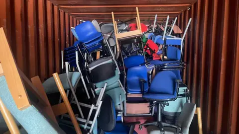 A shipping container filled with office chairs and desks.
