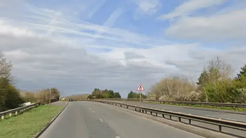A dual carriageway pinch a metallic obstruction down nan middle. There are greenish trees and writer either broadside pinch a bluish entity above.