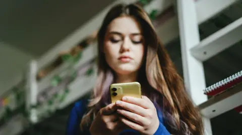 A young woman looks down at her mobile phone.
