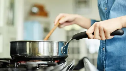 Women cooking with a frying pan over a gas hob