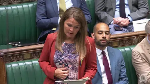 Vikki Slade speaking at the House of Commons. She is reading from a piece of paper. There are other MPs sitting behind her.