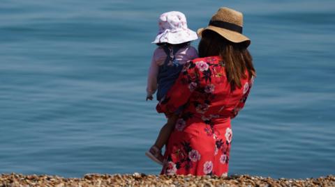 A woman holding a child looking at the sea