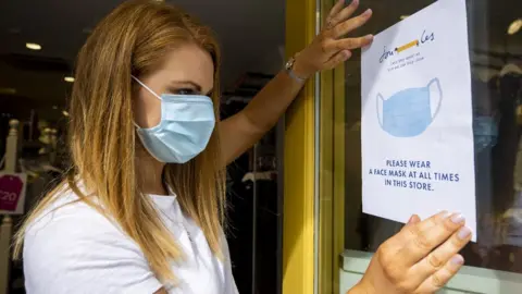 PA Media Shop owner holding up sign enforcing mask wearing in a shop
