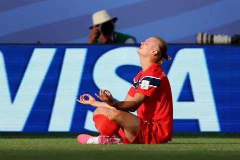 Getty Images Haaland sits cross legged on the ground with his hands rested atop his knees. His eyes are closed and he has a wide smile. 