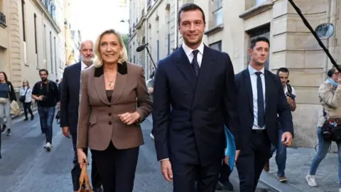 Reuters A woman in a brown jacket walks along side a younger man in a dark suit on the right