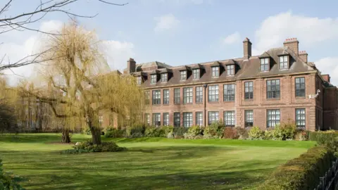 An image of the exterior of University of Hull, with lawns and trees outside, and a large red-brick building.