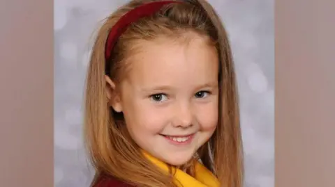 Family handout Elsie Dot Stancombe in a school picture wearing a read headband and smiling