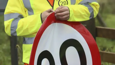 Alamy 20mph stickers being applied to speed signs in the Scottish Borders