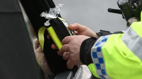 PA Media A police officer looking at a breathalyser