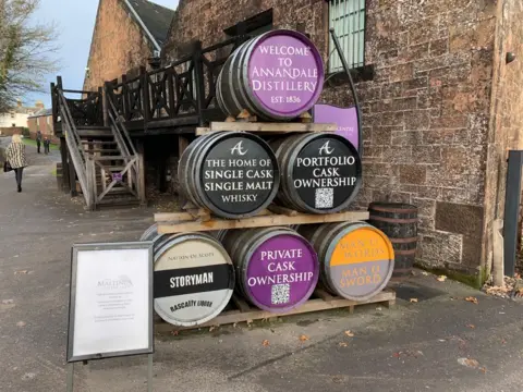 A selection of colourful whisky barrels on top of one another with the message Welcome to Annandale Distillery