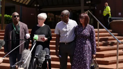PA Media Legal representatives for the Atkinson family read a statement alongside Kenroy Atkinson, brother of Dalian, and his wife Julie (R), outside Birmingham Crown Court.