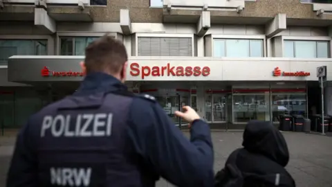 Reuters Policeman in uniform stands in front of a building that says Sparkasse on the front