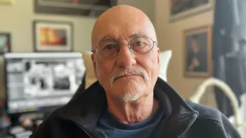 Alan Lodge looks at the camera. He wears glasses and a blue fleece.
