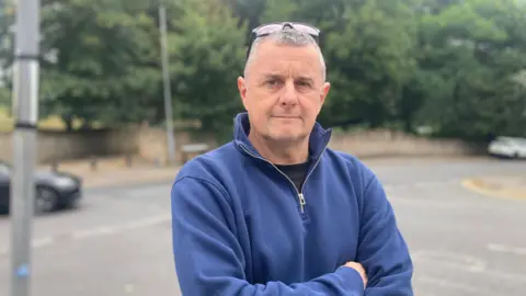 Sean Panting dressed in a blue fleece top with the collar up and his arms folded