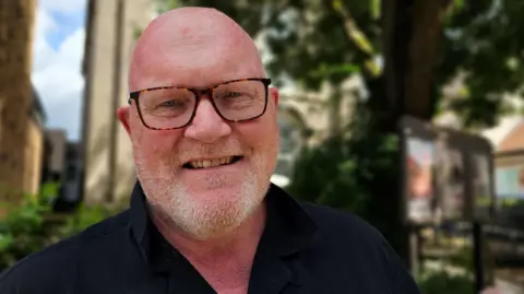 Paul Moseley/BBC A close-up picture of Terry Land. He's wearing rimmed glasses and a dark shirt on a sunny day.
