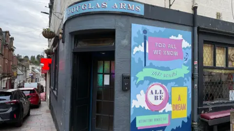 The outside of a pub with a mural to the right saying "for all we know this could all be a dream"