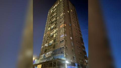 Night-time view of 18-storey block with scaffolding